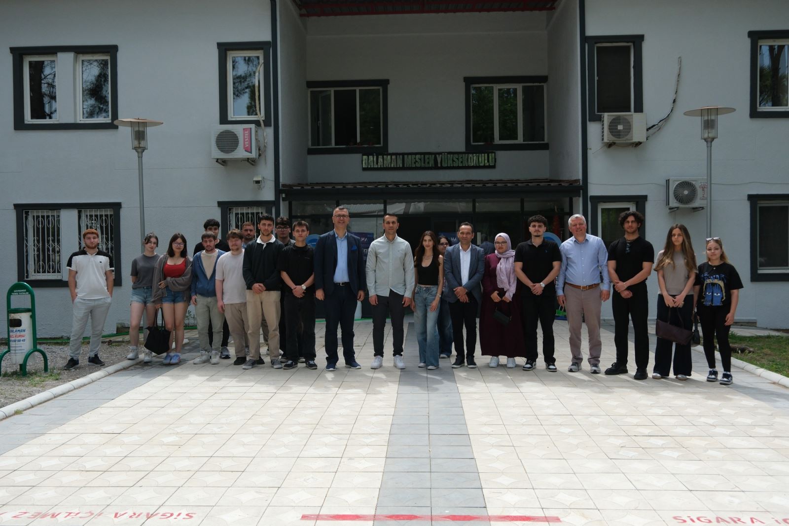 Students, academic staff and event participants are posing for a group photograph together in front of the Dalaman Vocational School building.
